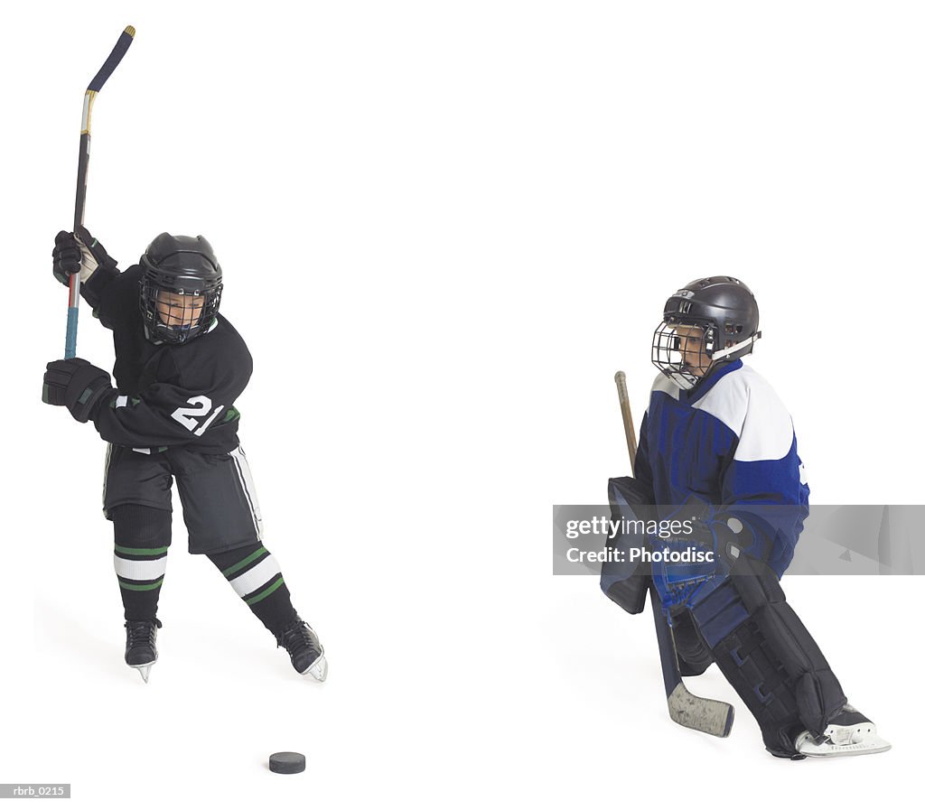 Two child caucasian male hockey players on opposing teams face off as one prepares to shoot as the goalie gets ready to block