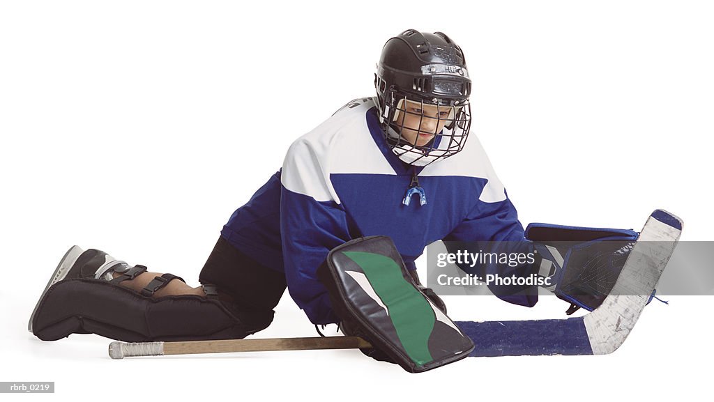 A child caucasian male hockey player in blue and white serving as goalie dives to the ground to block a shot