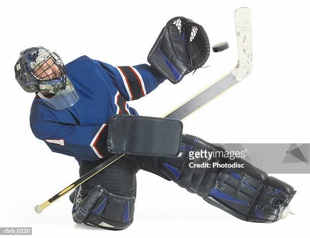 adult caucasian male hockey goalie kneels down and raises his arm to block a puck flying towards him - difensore hockey su ghiaccio foto e immagini stock
