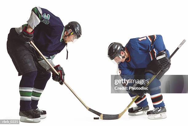 two adult caucasian male hockey players from opposing teams face off with their sticks for control of the puck - uniforme de hóquei no gelo imagens e fotografias de stock