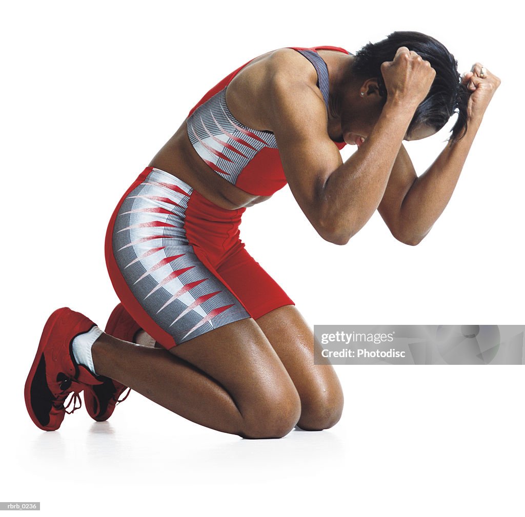 A young african american female runner kneels and grabs her head showing discouragement after losing a race