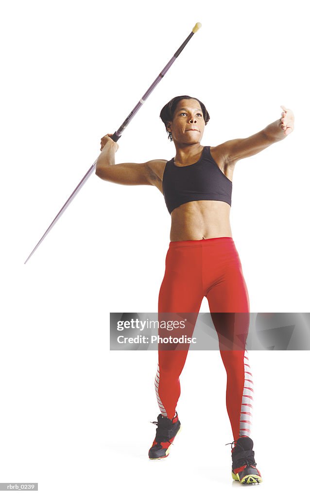 A young african american female athlete in red pants and a black sports bra pulls her arm back to release a javelin