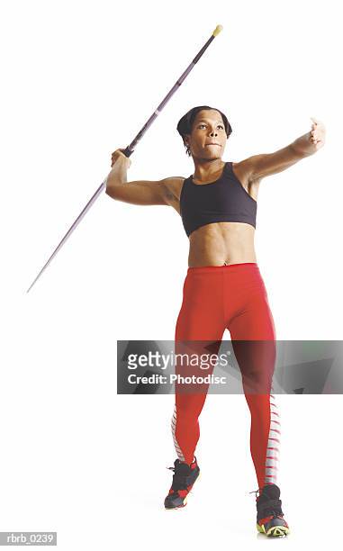 a young african american female athlete in red pants and a black sports bra pulls her arm back to release a javelin - womens field event stockfoto's en -beelden