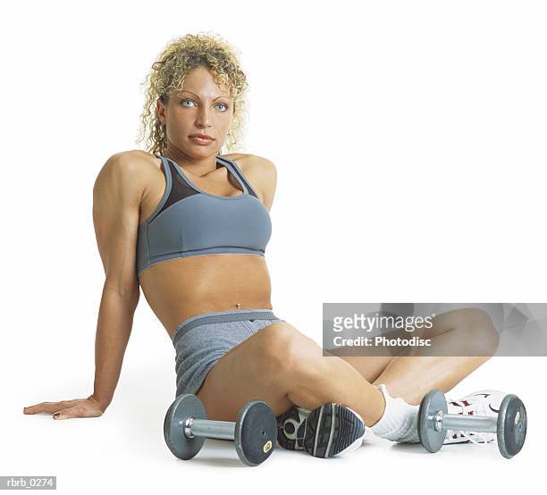 a curly haired blond female weightlifter is wearing gray and sitting cross-legged on the floor next to her dumb bells - curly stock pictures, royalty-free photos & images