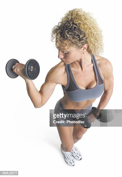 a blond female weight lifter with curly hair is wearing gray and lifting dumb bells as she looks to her right and the camera looks down on her - curly stock pictures, royalty-free photos & images