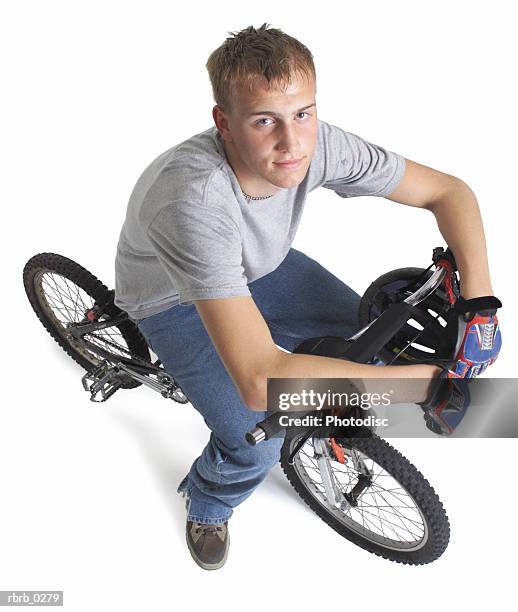 a blond caucasian teenage boy is sitting on his bike resting his hands on the handle bars as he looks up into the camera - bicycle top view stock-fotos und bilder