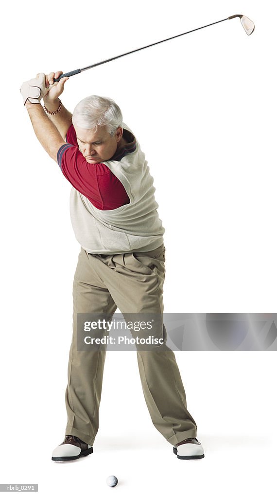 Caucasian middle aged man wears red and tan swings golf club over his head preparing to hit the ball