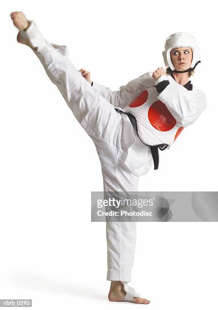 a caucasian female karate black belt dressed in white is wearing a protective vest with a red circle and kicking high to her right - karate belt stock pictures, royalty-free photos & images
