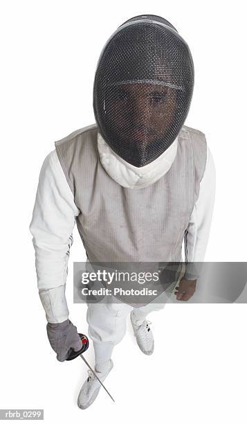 a male fencer holding a sword is dressed in gray and white while wearing a dark mesh mask and looking up at the camera - fäktningsmask bildbanksfoton och bilder