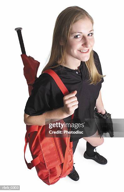 a pretty caucasian teenage girl wearing a black softball shirt is holding her softball gear in a red bag over her shoulder looking up at the camera - camera bag stock-fotos und bilder