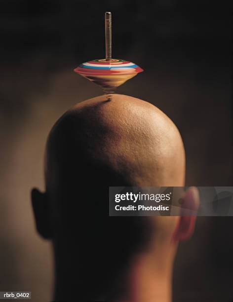 abstract conceptual photograph of a bald caucasian man spinning a top on his head - bald stock-fotos und bilder