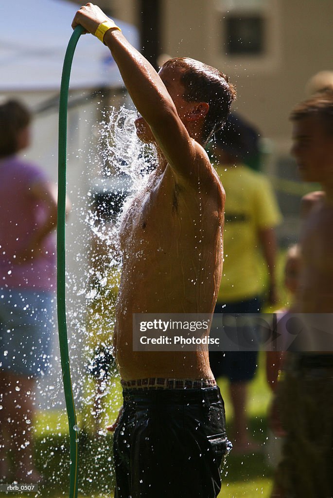 Lifestyle photo of a caucasian male child in a swimsuit as he sprays himself with a hose