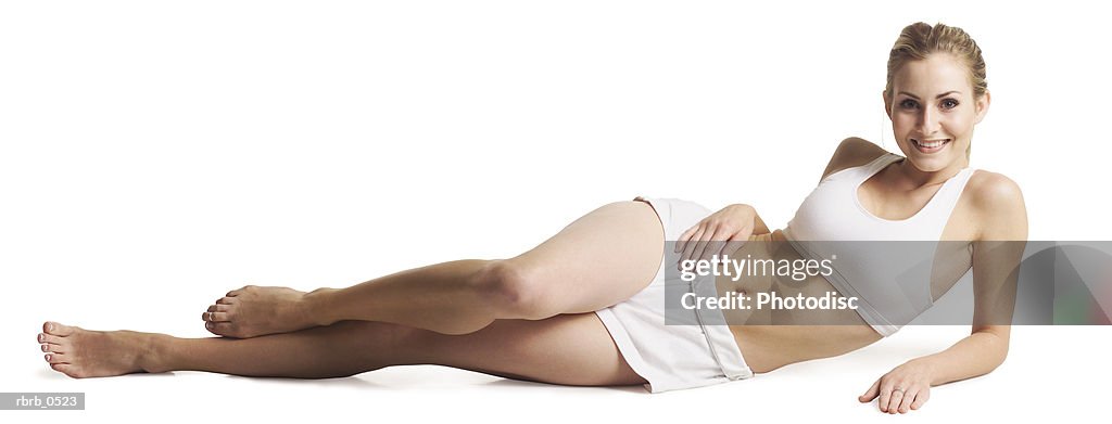 A young attractive caucasian female in a white work out outfit lays on her side and smiles