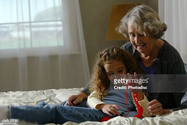 lifestyle portrait of a caucasian grandmother as she teaches her granddaughter to knit with yarn - old granny knitting stock pictures, royalty-free photos & images