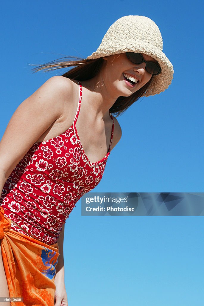 A young attractive caucasian female in a swimsuit hat and sunglasses plays at a beach