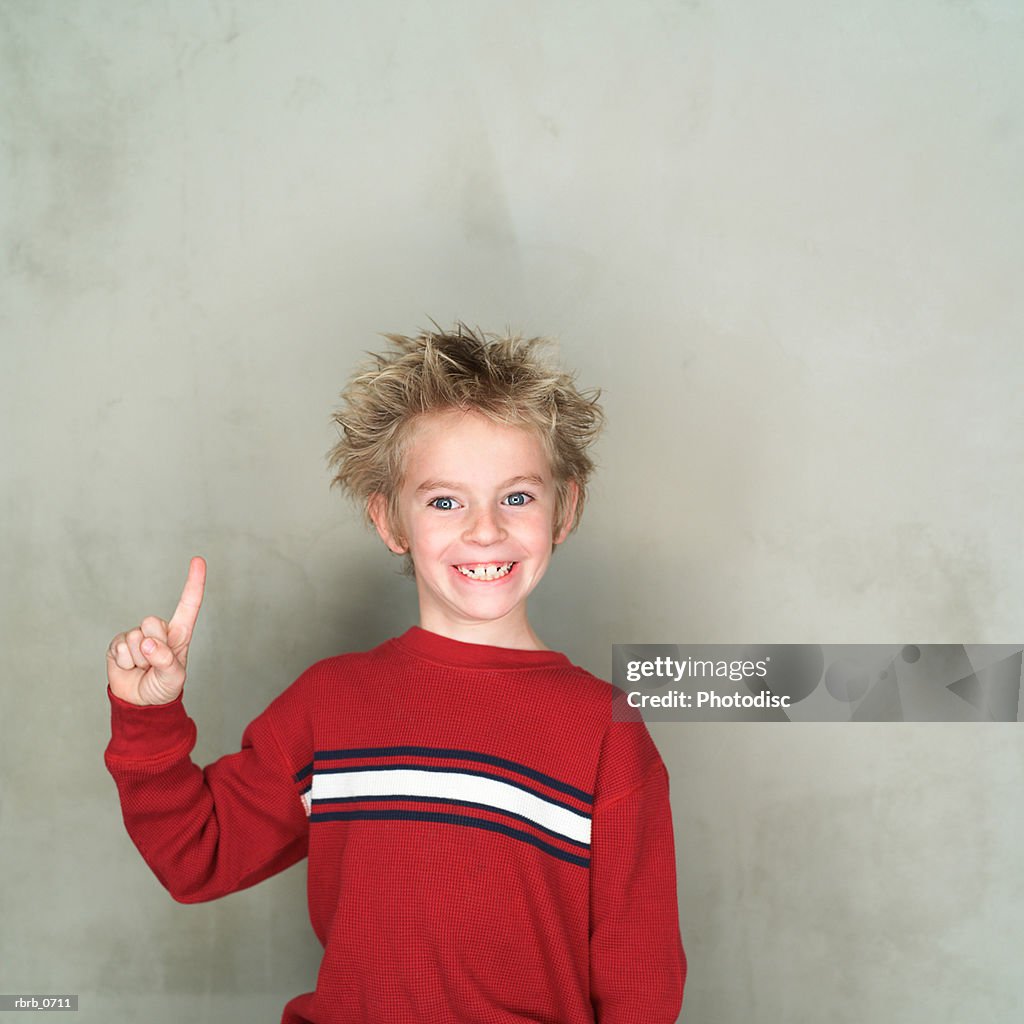 Portrait of a caucasian male child in a red shirt as he points upward and smiles