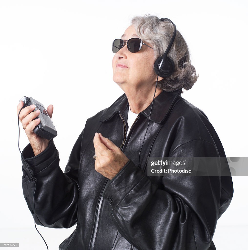 Portrait of an elderly caucasian woman in a leather jacket and sunglasses as she listens to music through headphones