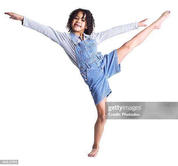 silhouette of an african american little girl in denim overalls as she kicks up high into the air - high up ストックフォトと画像