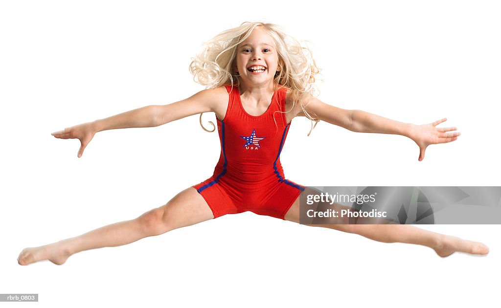 Silhouette of caucasian blonde female child dancer in a red outfit as she jumps and does the splits
