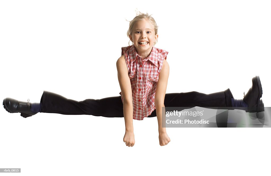 Silhouette of a caucasian blonde female child  in black pants and a plaid shirt as she jumps up and does the splits