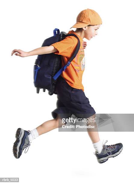 a caucasian little boy with an orange ballcap and a backpack runs along to school - sac à dos enfant photos et images de collection