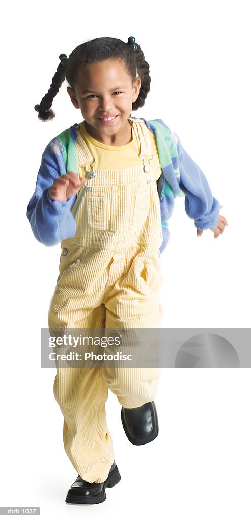 A cute little african american girl in yellow overalls playfully runs forward and smiles