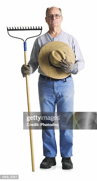 an elderly male farmer with a hat and rake glares sternly into the camera - strohhut freisteller stock-fotos und bilder