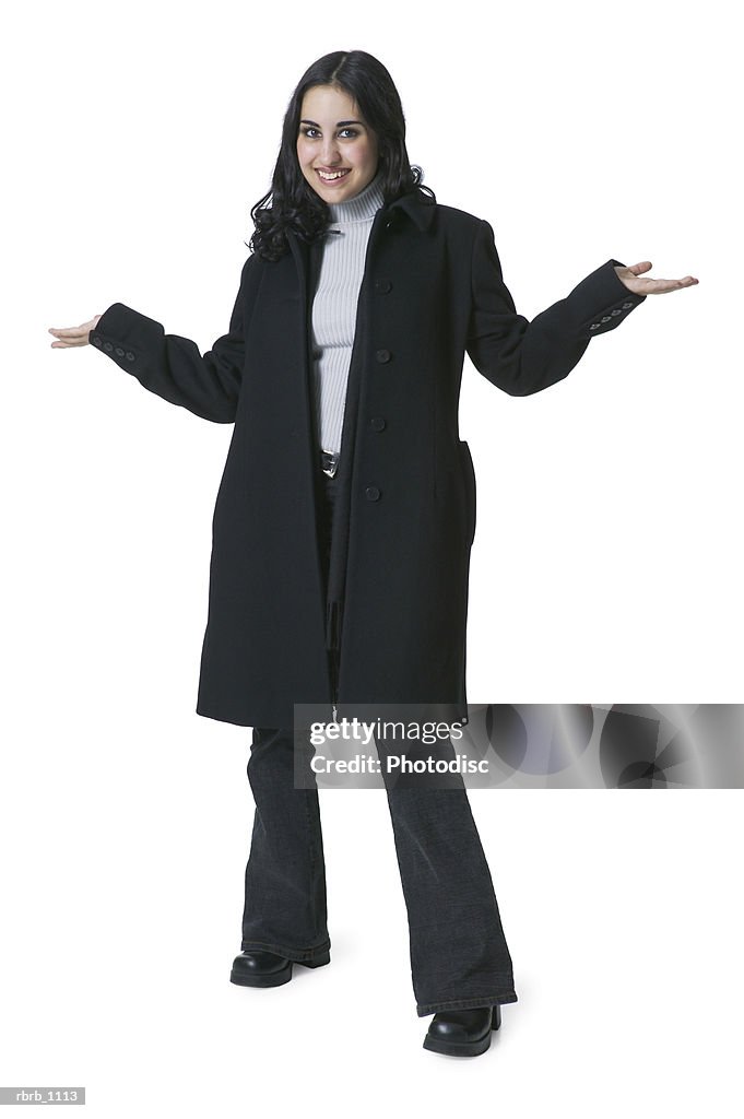 A young hispanic woman in a long black coat smiles as she shrugs her shoulders