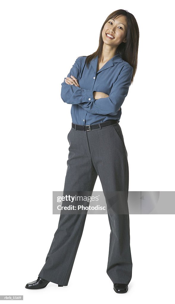An adult asian woman in grey pants and a blue shirt folds her arms and smiles