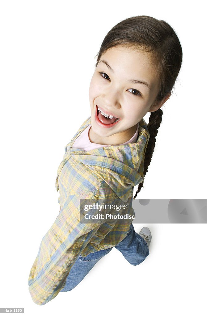 An asian female child in jeans and a green shirt bends around as she smiles up at the camera