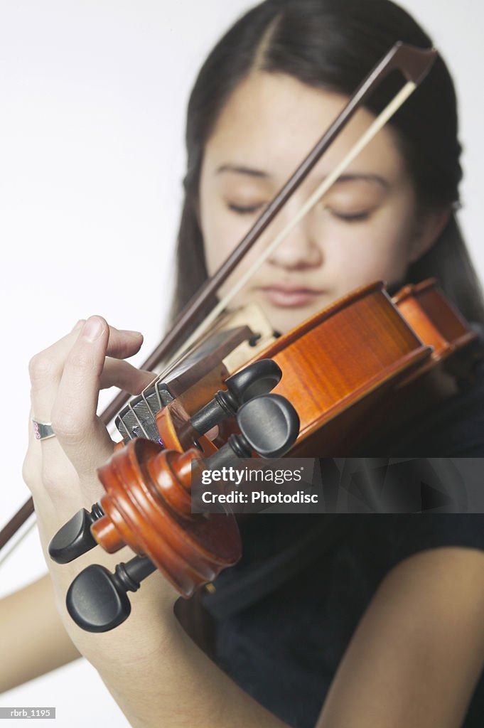 Portrait of an asian female teen as she plays her violin and closes her eyes