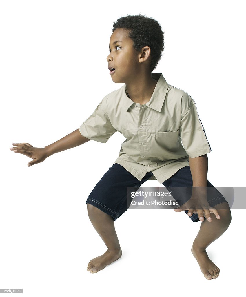 An african american male child in black shorts and a tan shirt strikes a fun surfing pose