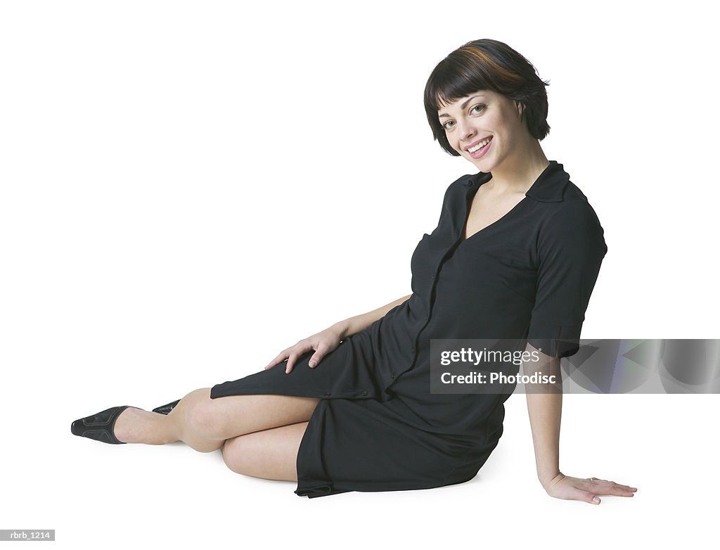 A young caucasian brunette woman in a black dress sits on her side and smiles