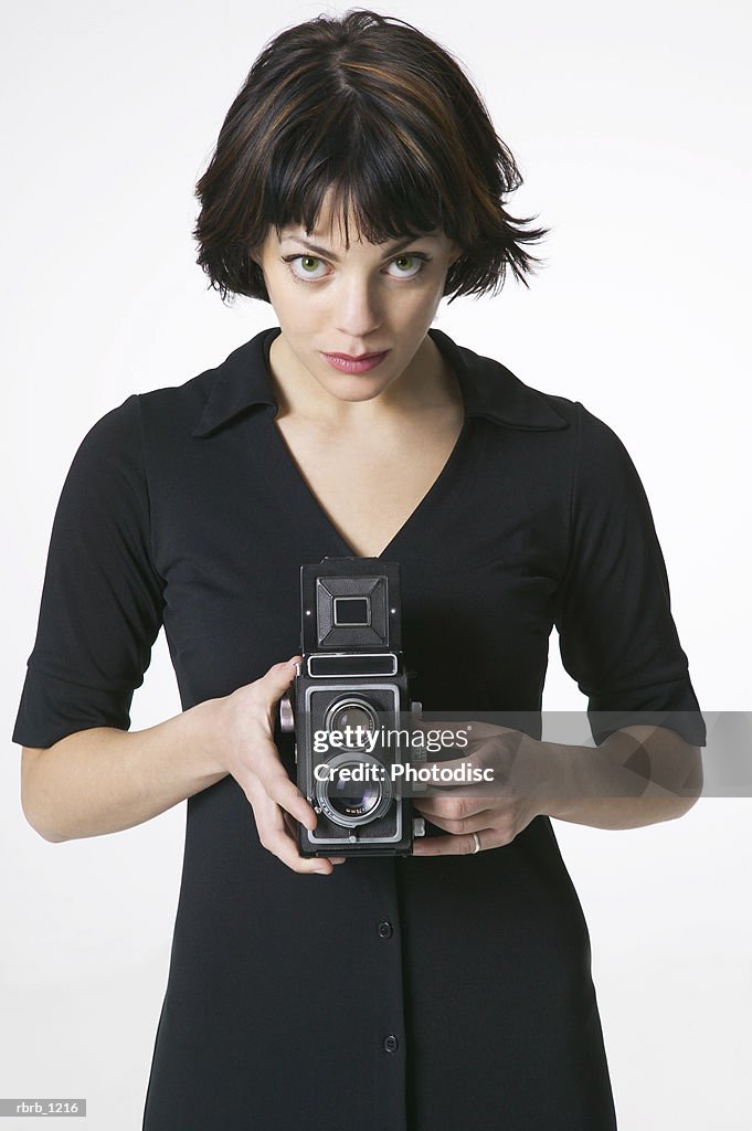 Portrait of an attractive brunette woman in a black dress stands using an old camera