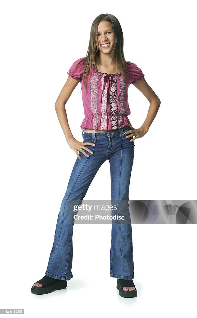 A caucasian teenage female in a jeans and a pink shirt puts her hands on her hips and smiles