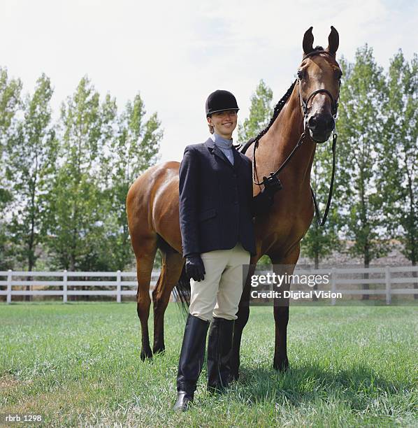 a young caucasian female horseback rider poses with her horse and smiles - equestrian helmet stock pictures, royalty-free photos & images