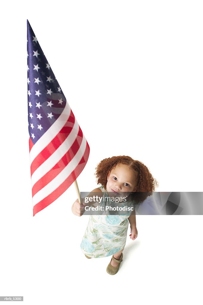 A cute redheaded female child in a green dress holds up an amercian flag to the camera