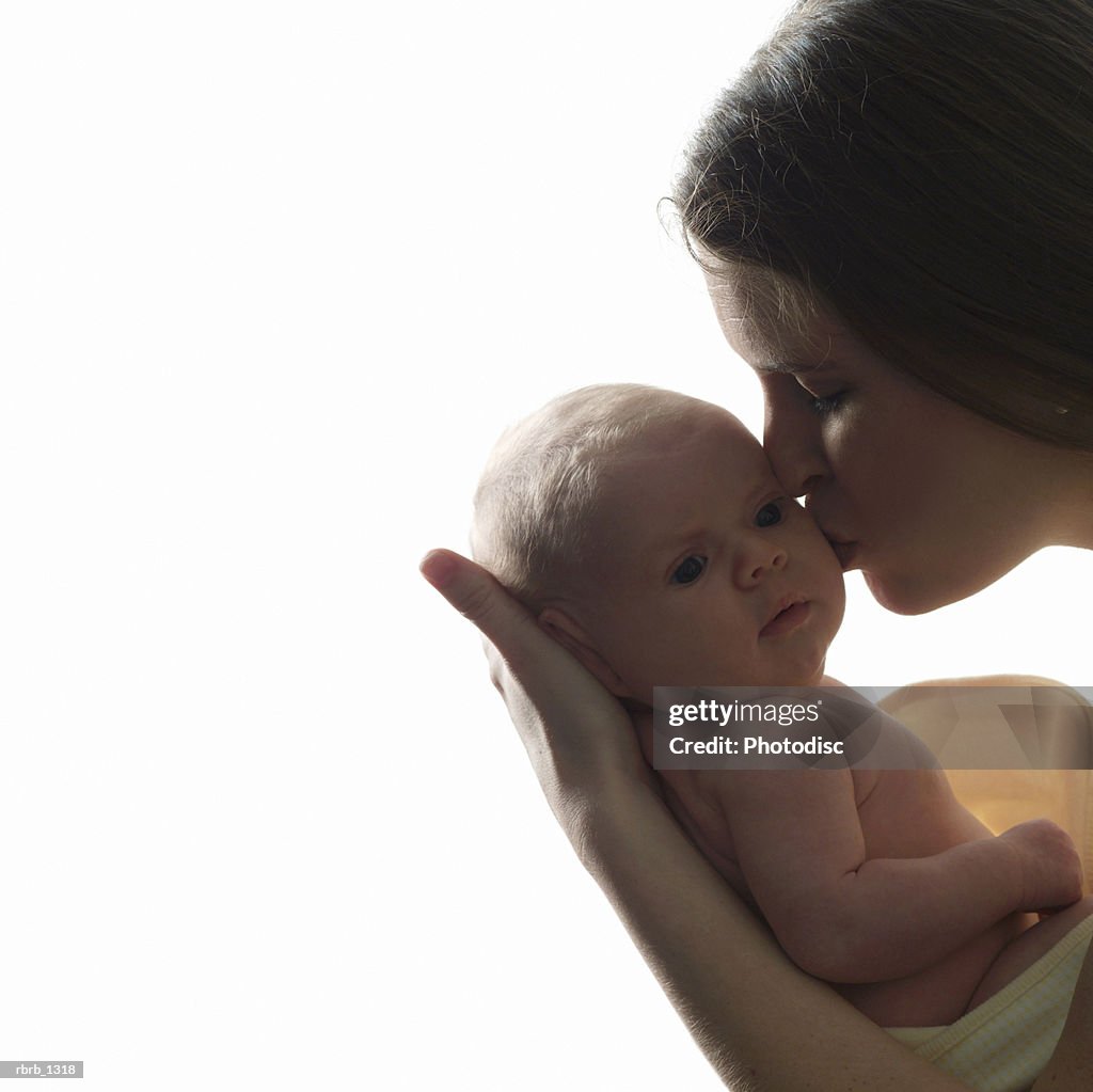 Portrait of a young caucasian mother leaning in and kissing her newborn baby