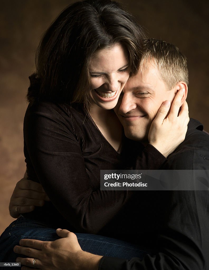 Studio portrait of a young caucasian couple as the woman lovingly hugs the man as they laugh