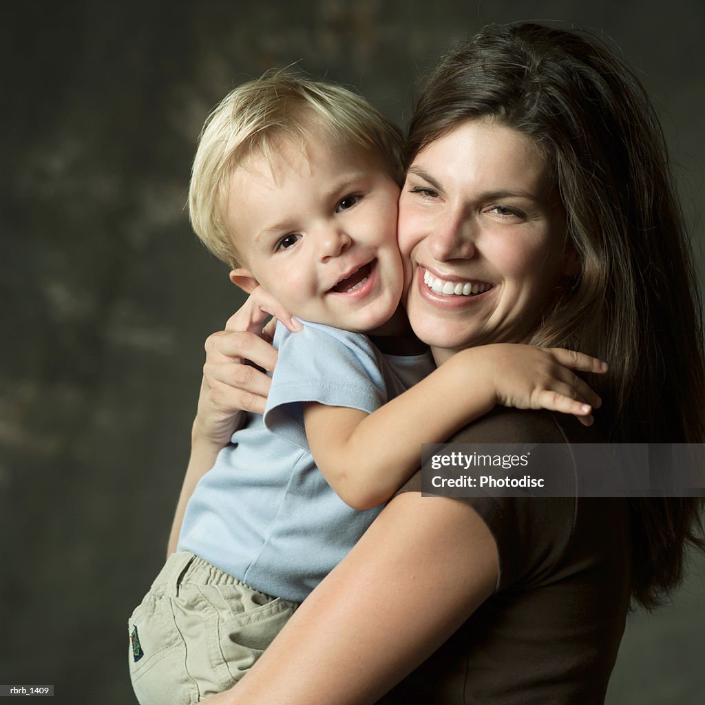 Studio portrait of a caucasian brunette mother holds her young blonde son as they both laugh