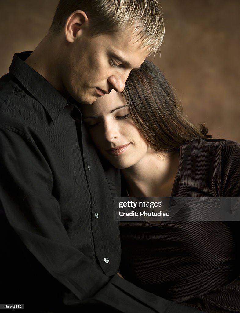 Studio portrait of a caucasian couple as the woman rests her head on the shoulder of the man