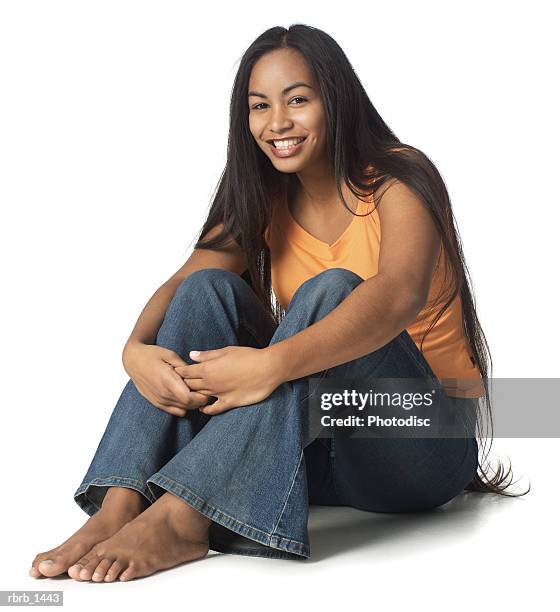 an ethnic female teenager in jeans and an orange shirt sits down and smiles brightly - one teenage girl only imagens e fotografias de stock