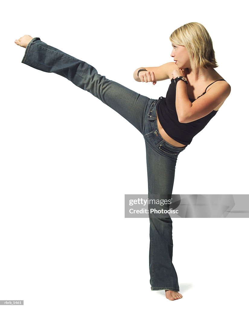 A young caucasian blonde woman in jeans and a black tank top strikes a martial arts pose