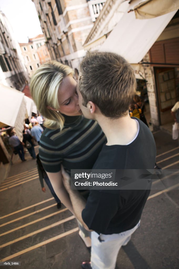 A young caucasian couple embrace and kiss while standing in a european marketplace