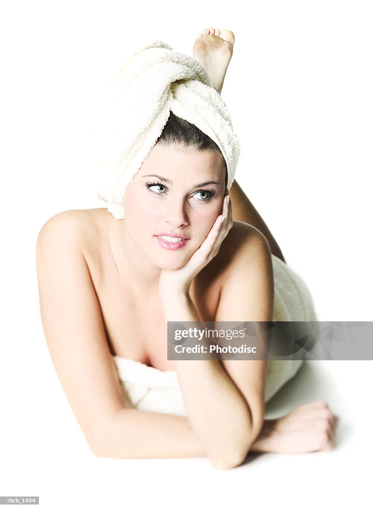An attractive young caucasian woman with a towel on her head lays down and smiles slightly