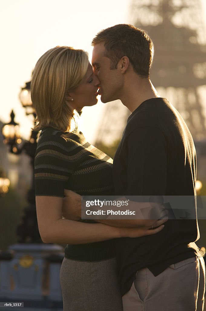 A young attractive caucasian couple embrace and kiss at the eiffel tower in paris