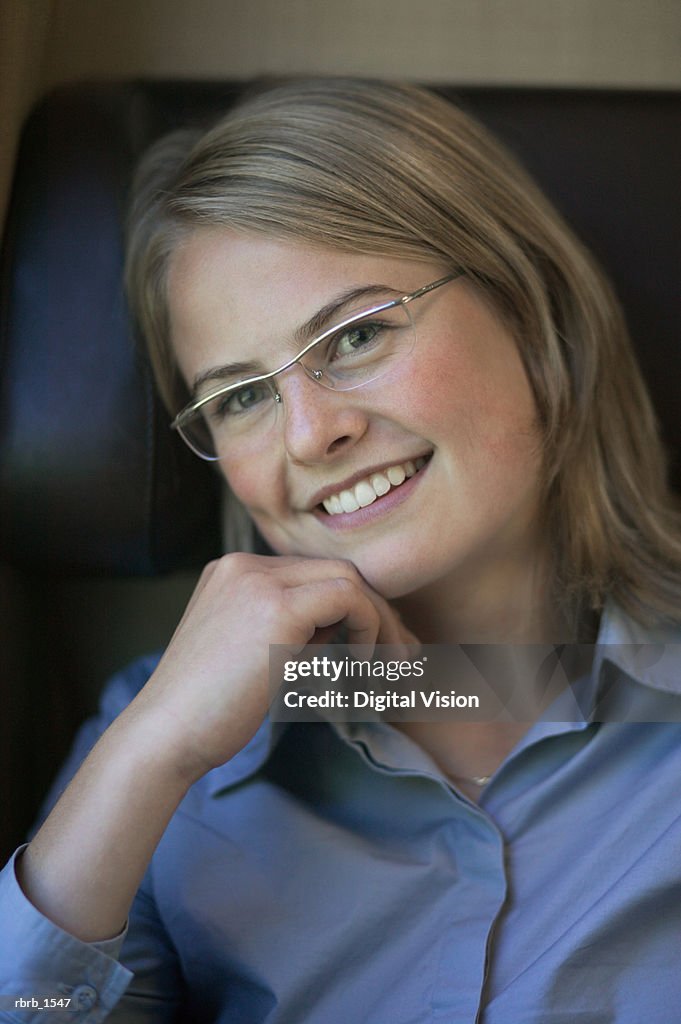 A young caucasian blonde woman in a blue shirt and glasses smiles playfully