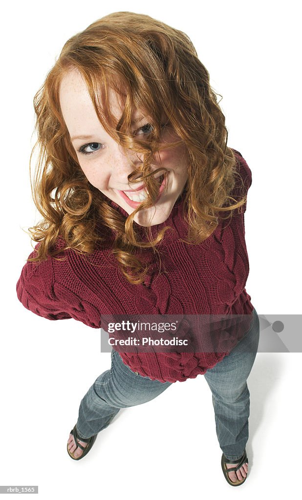 A caucasian redheaded female teen in jeans and a red sweater smiles up at the camera