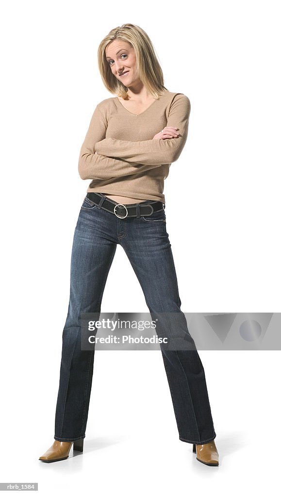 A young caucasian blonde woman in jeans and a tan shirt folds her arms and smilies