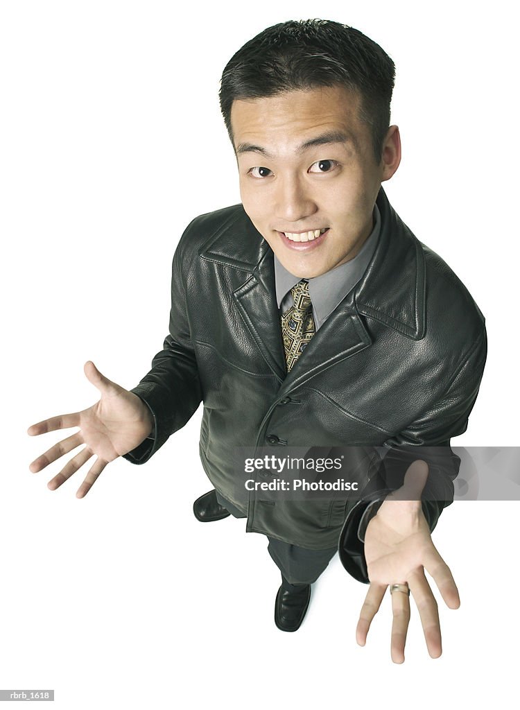 An adult asian business man in a leather jacket gestures with his hands and smiles up at the camera